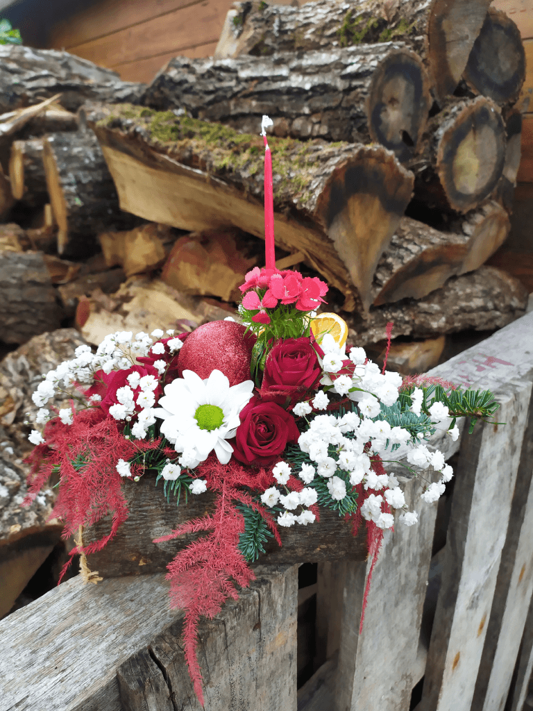 Composition florale piquée et réalisée dans un tronc d’arbre creusé, réalisé avec des roses rouges, des gypsophiles, des branches de sain et orné d'une fine bougie rouge et de quelques tranches d'agrumes séchées