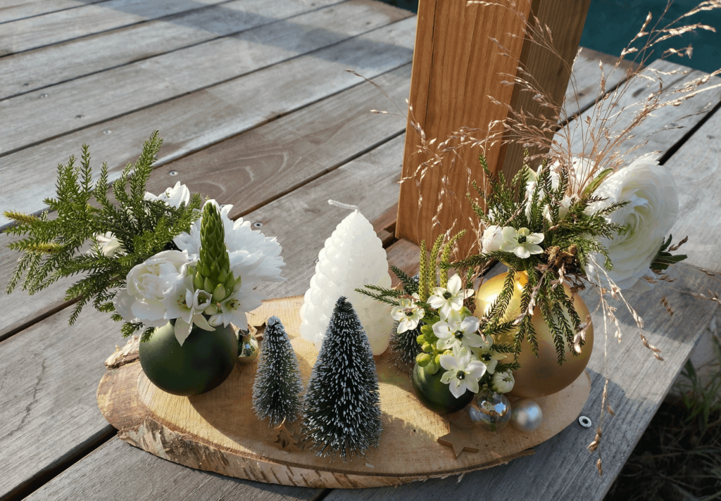 Composition pour Noël réalisée avec des boules de Noël détournées comme petits vases, décorations de Noël, l'ensemble collé sur une section de tronc de bouleau.