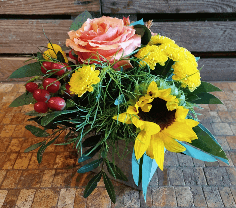 Les Compos de Pauline : composition florale dans les règles de l'art au ton chatoyant du soleil : Tournesol, Chrysanthèmes jaune vif, Millepertuis et gros bouton de Rose saumon.